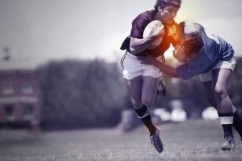 Two rugby players collide mid-air during a match on a grassy field.